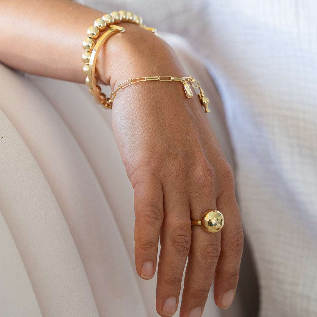 Hand wearing gold bracelets and a ring on a white background