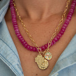 Necklace with pink beads and gold chain worn by a person, with a blue denim shirt in the background.