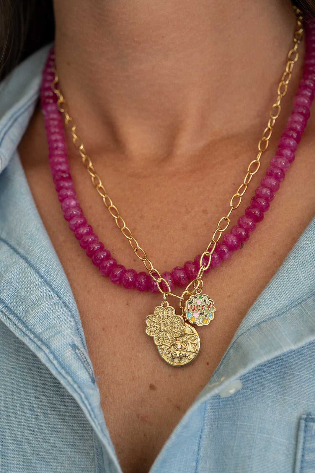 Necklace with pink beads and gold chain worn by a person, with a blue denim shirt in the background.