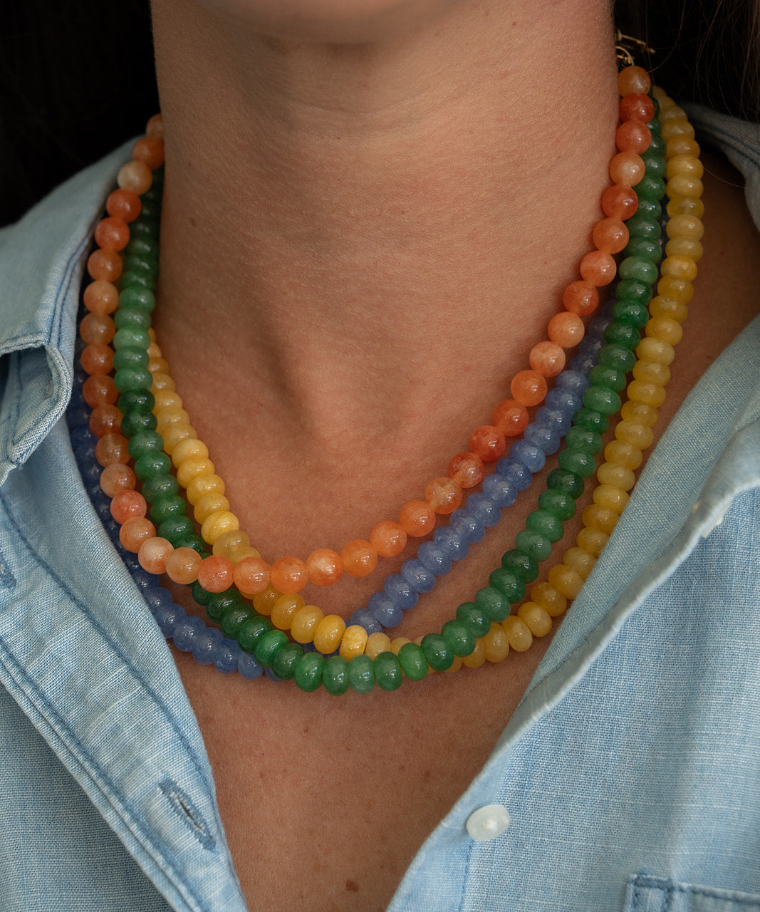 Close-up of a person wearing a colorful beaded necklace with a light blue shirt.