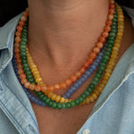 Close-up of a person wearing a colorful beaded necklace with a light blue shirt.