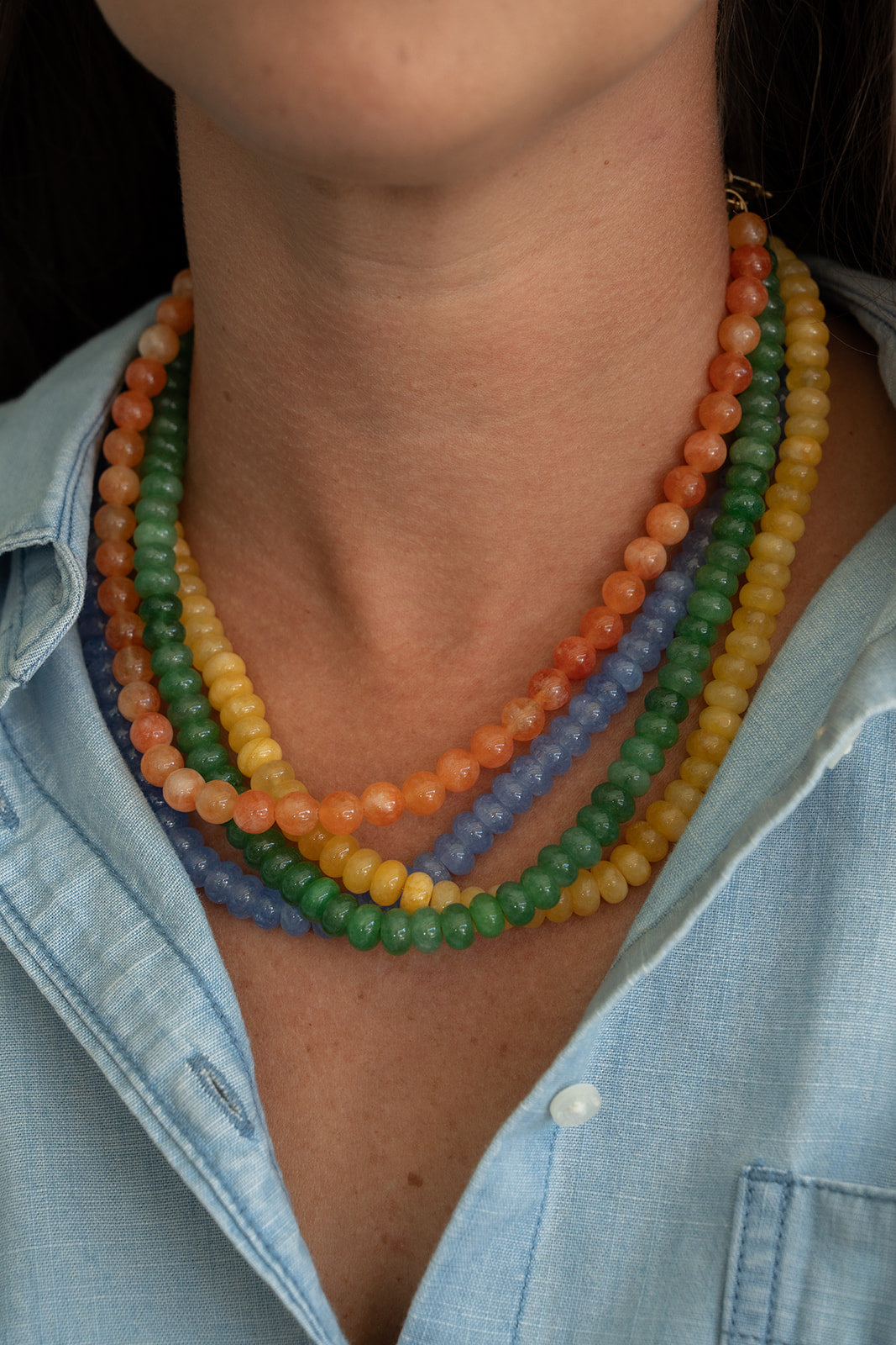Close-up of a person wearing a colorful beaded necklace with a light blue shirt.