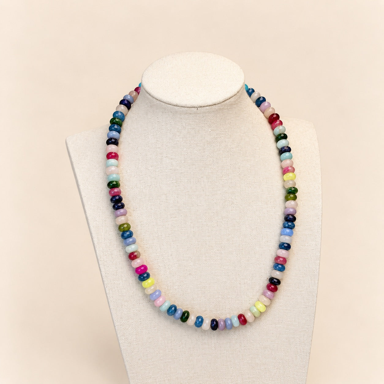 A colorful beaded necklace displayed on a cream fabric jewelry bust against a light beige background.