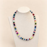A colorful beaded necklace displayed on a cream fabric jewelry bust against a light beige background.